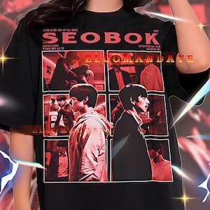 May include: Black unisex t-shirt featuring the movie title "SEOBOK" in red, along with images from the film. The shirt also includes the text "ELCOMANDATE" and the names of the actors and director.