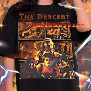 May include: Black unisex t-shirt featuring a movie poster design for "The Descent." The design includes the film's title, cast, and imagery from the horror film. The shirt is a 2XL size.
