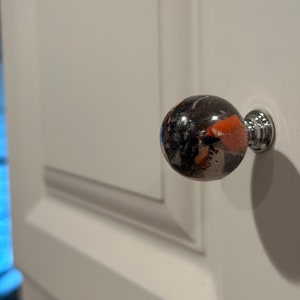 Può includere: Un pomello per armadio rotondo, nero, arancione e bianco con una base argentata.