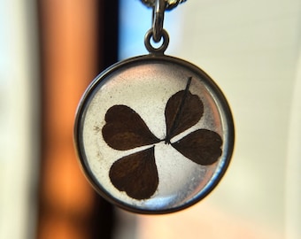 May include: A silver chain necklace with a clear pendant containing a pressed four-leaf clover.