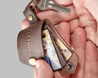 May include: Brown leather keyring with a photo holder and the word "DADDY" embossed on the front. The keyring has a silver key ring and a silver key attached.