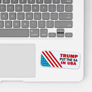 May include: A white sticker with the text "TRUMP PUT THE SA IN USA" in red letters. The sticker has a blue section with white stars and red stripes, resembling the American flag, and is placed on a laptop.