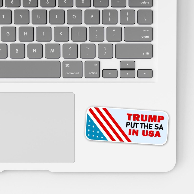 May include: A white sticker with the text "TRUMP PUT THE SA IN USA" in red letters. The sticker has a blue section with white stars and red stripes, resembling the American flag, and is placed on a laptop.