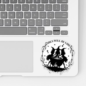 May include: Black and white sticker with a circle design featuring three witches in silhouette standing around a cauldron. The text "GIRLS WILL BE GIRLS" is written around the circle.