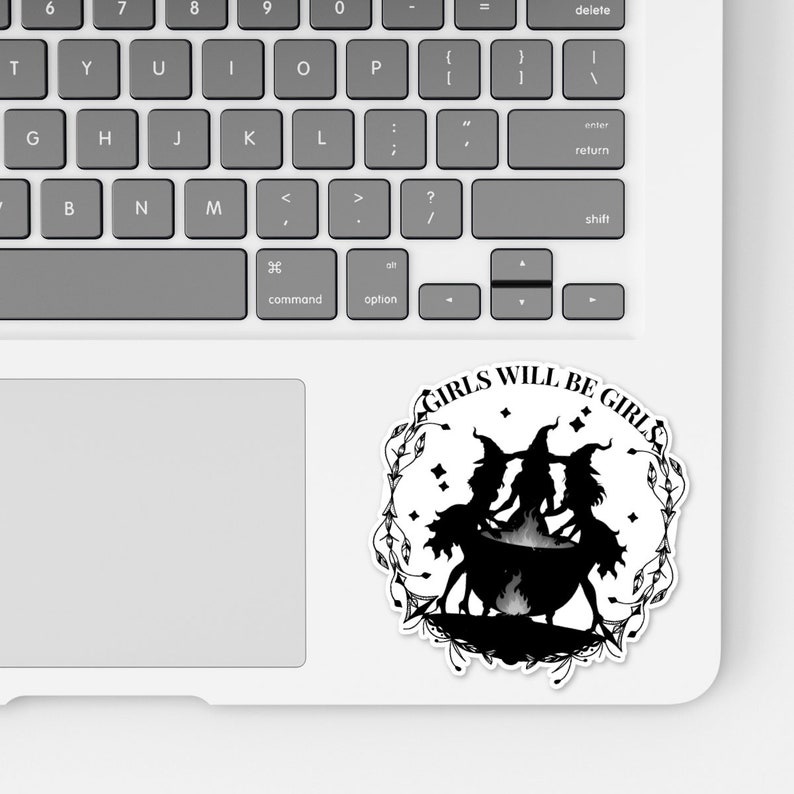 May include: Black and white sticker with a circle design featuring three witches in silhouette standing around a cauldron. The text "GIRLS WILL BE GIRLS" is written around the circle.