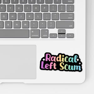 May include: A sticker with the text "Radical Left Scum" in a rainbow gradient font, outlined in black, on a white laptop. The laptop keyboard is visible.