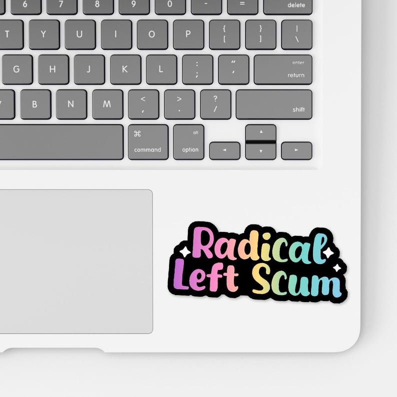 May include: A sticker with the text "Radical Left Scum" in a rainbow gradient font, outlined in black, on a white laptop. The laptop keyboard is visible.