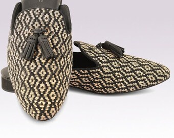 May include: A pair of black and beige patterned slippers with tassels. The slippers feature a geometric pattern and are made from a woven material.