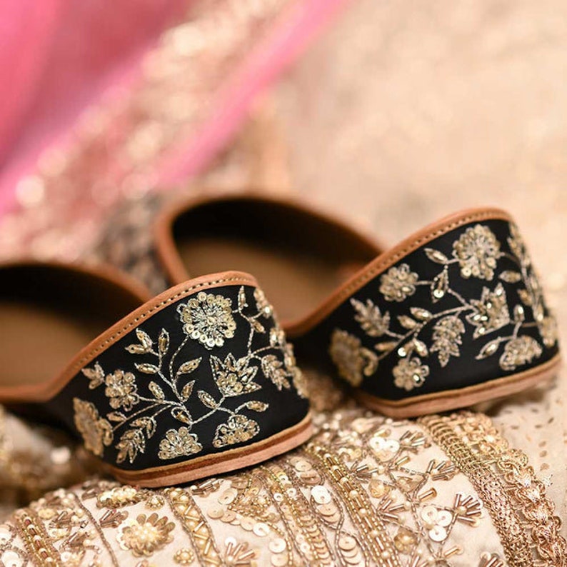 May include: A pair of black embroidered flat shoes with gold thread detailing. The shoes have a brown leather trim and are decorated with floral patterns.