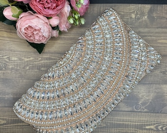 May include: A gold clutch purse covered in clear and iridescent rhinestones. The purse is decorated with a pattern of concentric circles.
