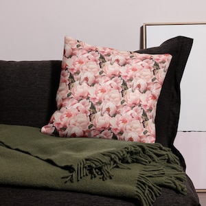 Może przedstawiać: Poduszka dekoracyjna z kwiatowym wzorem przedstawiającym różowe piwonie na ciemnym tle. Poduszka leży na ciemnobrązowej sofie z zielonym kocem.