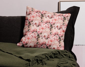 May include: A throw pillow with a floral pattern featuring pink peonies on a dark background. The pillow is sitting on a dark brown couch with a green throw blanket.