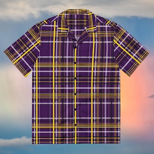 Può includere: Una camicia a maniche corte con bottoni e un motivo a quadri nei toni del viola, giallo, bianco e marrone scuro. La camicia presenta un colletto a revers, un orlo dritto e una fila verticale di bottoni scuri lungo l'abbottonatura frontale.