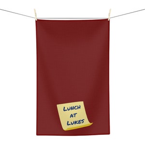 May include: A red kitchen towel hangs on a washing line with a yellow sticky note that says "LUNCH AT LUKES"
