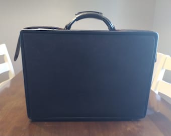 May include: A black leather briefcase with a metal handle. The briefcase has a smooth, textured surface.