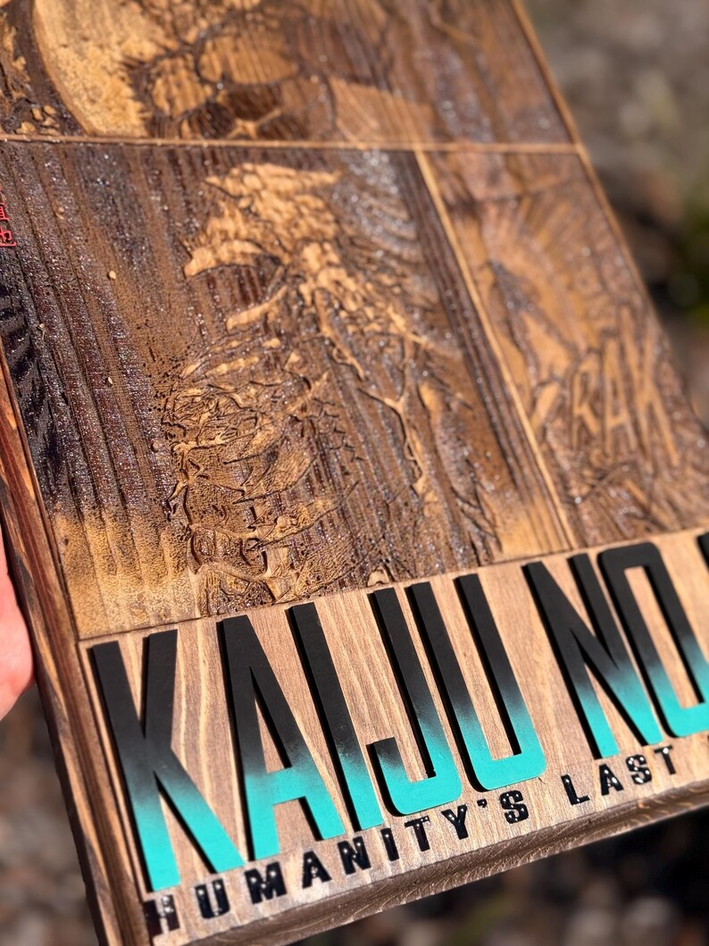 Puede incluir: Un letrero de madera con un dise&ntilde;o tallado y las palabras "KAIJU NO" en letras negras grandes con un degradado turquesa. Debajo, se muestra el texto "HUMANITY'S LAST". El letrero tiene un acabado marr&oacute;n oscuro.