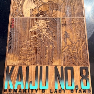 Puede incluir: Placa de madera con una ilustraci&oacute;n estilo c&oacute;mic. La obra de arte representa un gran monstruo y una figura en un paisaje rocoso. Las palabras "KAIJU NO. 8" est&aacute;n en letras negras grandes con un degradado turquesa, y "HUMANITY'S LAST STAND" debajo.