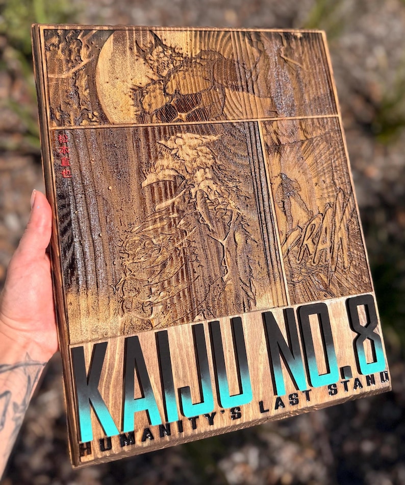Puede incluir: Obra de arte de madera con una ilustraci&oacute;n tallada de un monstruo de la serie de manga Kaiju No. 8. La obra incluye el texto "KAIJU NO. 8" en negro y turquesa, y "HUMANITY'S LAST STAND".