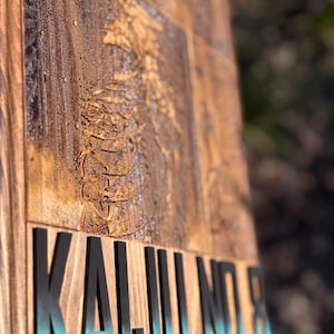 Puede incluir: Un letrero de madera con las palabras "KAIJU NO.8" en letras negras con un degradado turquesa. El letrero tiene un dise&ntilde;o tallado y el texto "HUMANITY'S LAST STAND" en la parte inferior. La madera tiene una veta natural y un tinte oscuro.