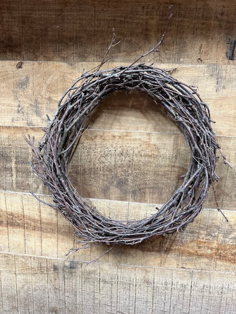 May include: A brown twig wreath, made of natural branches, is hanging on a wooden wall.