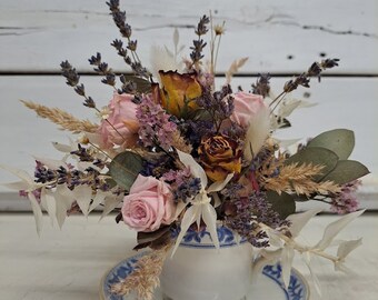May include: Dried flower arrangement in a white teacup with a blue and white pattern. The arrangement includes pink roses, dried lavender, and other dried flowers.
