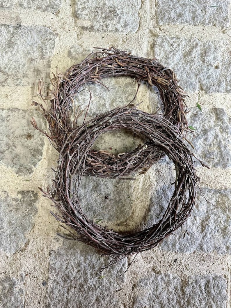 May include: Two brown twig wreaths, one smaller than the other, are stacked on top of each other on a light gray stone surface.