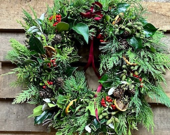 May include: A green Christmas wreath with red berries, dried orange slices, pine cones, and a burgundy ribbon.