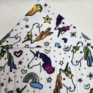 May include: White fleece hanging hammock with a rainbow unicorn print. The hammock has a fringe border and a black loop for hanging.