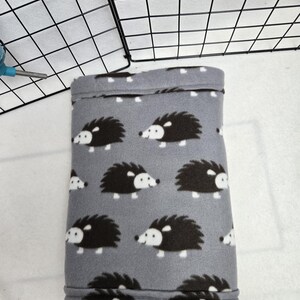 May include: A gray fleece hedgehog-patterned pet bed with white stitching around the edges.