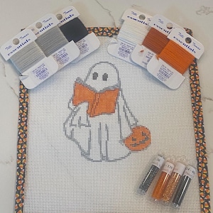 May include: A Halloween-themed needlepoint canvas featuring a ghost holding a pumpkin and wearing an orange scarf. The canvas is surrounded by a candy corn border, with spools of thread and beads in coordinating colors.