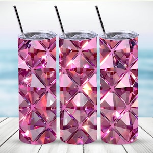May include: Three pink diamond-patterned tumblers with silver lids and straws. The tumblers have a faceted design that catches the light, creating a sparkling effect. The background is a blurred image of the ocean and a wooden surface.