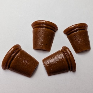May include: Four small, brown, decorative pot-shaped objects with a glossy finish. Each pot has a rounded rim and a slightly tapered body. The objects are arranged on a white surface, with slight variations in their orientation.