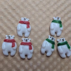 May include: Six small, white polar bear figurines with black eyes and noses. Three bears wear red scarves, and three wear green scarves. The bears are on a light brown surface.