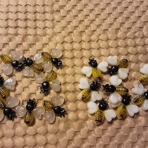 May include: Several small, decorative bee-shaped objects with yellow and black striped bodies, black heads, and white wings. The bees are arranged on a textured, honeycomb-patterned surface. The bees are likely used for crafting or decoration.