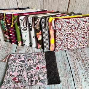 Peut inclure: Une collection de pochettes zippées aux motifs et couleurs variés. Les motifs comprennent des scènes florales, géométriques et forestières avec des animaux et des champignons. Certaines pochettes ont une section tricotée grise ou marron.