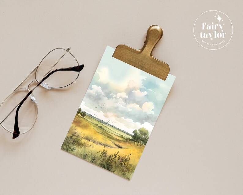 May include: A watercolour painting of a field with tall grass and a cloudy sky. The painting is on a white background and is framed by a gold clip.