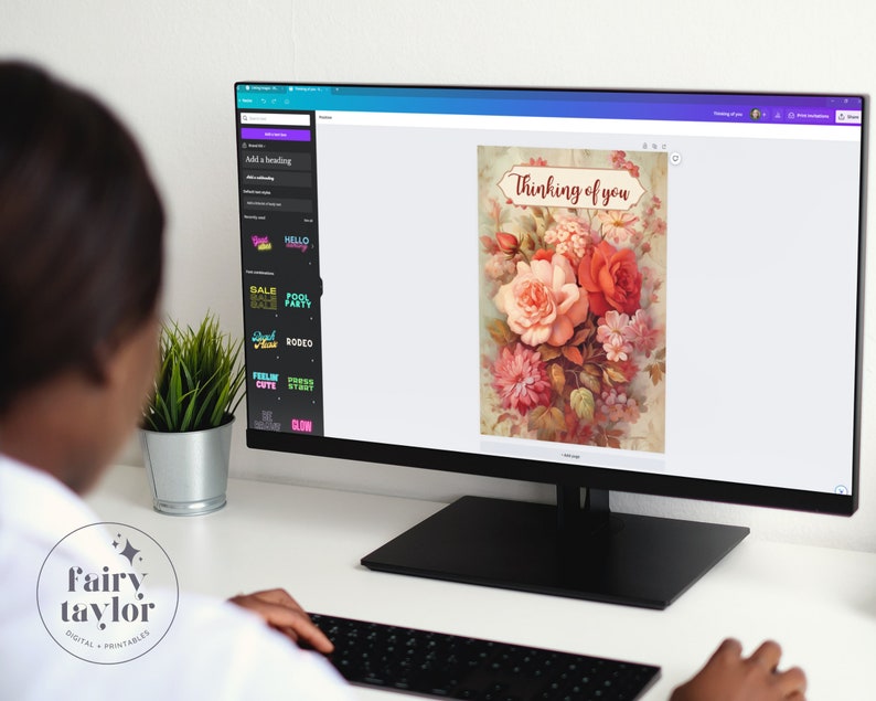 May include: A computer monitor displays a digital floral design with the text "Thinking of you." The design features a bouquet of roses and other flowers in shades of red, pink, and peach. The monitor is on a desk with a keyboard and a small potted plant.