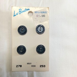May include: A card of four round navy blue buttons with two holes and a decorative etched border. The card is labeled Le Bouton, includes the text WAL-MART, 278, NAVY, HOOK, and 253, and features a circular hole at the top for hanging display.