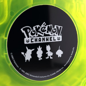 May include: A black GameCube game disc with a white Pokemon Channel logo and silhouettes of Pokemon characters. The text reads "© 2003 Pokémon. © 1995-2003 Nintendo/Creatures Inc./GAME FREAK inc. Developed by Ambrella."