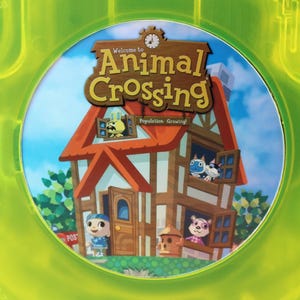 May include: A green game case with a circular disc inside. The disc features a cartoon house with a red roof and the text "Welcome to Animal Crossing Population: Growing!"