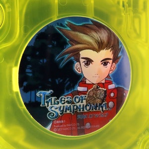May include: A yellow GameCube game case with a circular sticker featuring a cartoon character with brown hair and a red shirt. The sticker says "Tales of Symphonia" and "Tales of Symphonia".