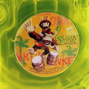 May include: A yellow GameCube disc with a Donkey Konga game disc inside. The Donkey Konga disc features Donkey Kong and Diddy Kong playing bongos with a tropical background.