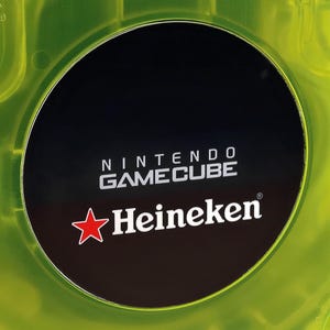 Peut inclure: Un disque noir de Nintendo GameCube avec le texte "NINTENDO GAMECUBE" et "Heineken" en lettres blanches. Le disque est entouré d'un boîtier en plastique jaune vif.