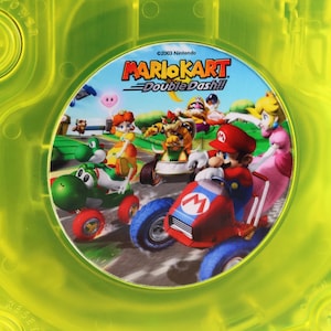 May include: A yellow GameCube game disc case with a circular image of Mario Kart Double Dash!! characters. The image features Mario, Luigi, Yoshi, Peach, and Bowser.
