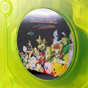 May include: A green GameCube game case with a black disc featuring the text "SUPER SMASH BROS. MELÉE" and a colorful image of various video game characters.