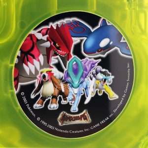 Pode incluir: Um close-up de um cartucho de jogo Game Boy Advance preto e verde com um rótulo circular apresentando vários personagens Pokémon. O rótulo inclui o texto "© 2003 Pokémon, © 1995-2003 Nintendo/Creatures Inc./GAME FREAK inc. Developed by Genius Sonority Inc."