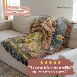 May include: A woven throw blanket featuring a whimsical frog design. The blanket showcases a frog wearing a floral dress, surrounded by flowers in shades of green, yellow, and pink. The text "HIGH QUALITY 100% COTTON YARN" is visible. The blanket is draped over a beige sofa.