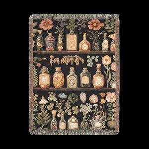 Op de afbeelding: Een geweven tapijtdeken met een zwarte achtergrond met daarop een vintage apotheekrek met rijen glazen flessen gevuld met kleurrijke vloeistoffen. De flessen zijn omringd door verschillende botanische illustraties van bloemen, bladeren en kruiden.
