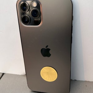 Puede incluir: Un iPhone negro con una pegatina dorada de una persona con los brazos extendidos en la parte posterior.