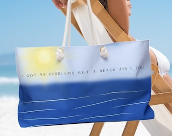 May include: A blue and white beach tote bag with the text "I got 99 problems but a beach ain't one". The bag is sitting on a wooden beach chair.